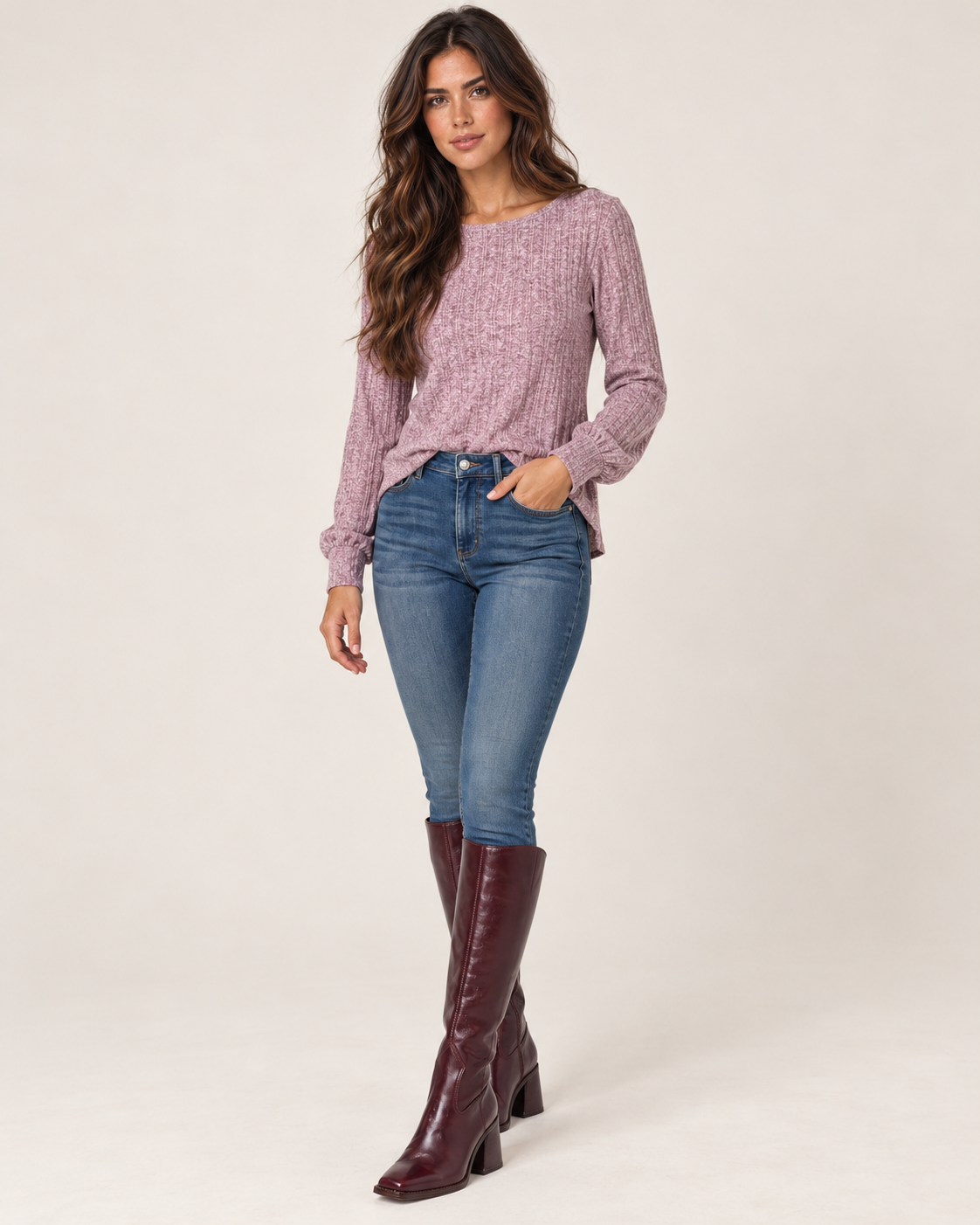 Side view of a woman wearing a dusty mauve lightweight crewneck sweater with long sleeves and blue jeans on a beige background.