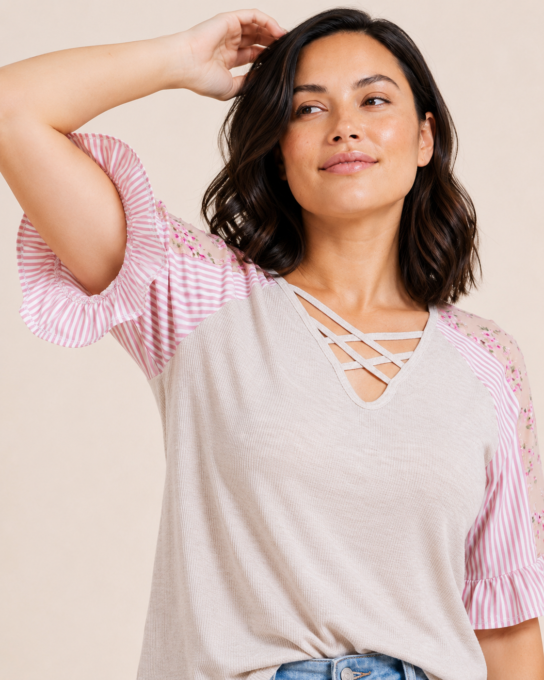 Close-up of a woman wearing a blush cross-front tee with floral puff sleeves and light wash denim jeans on a beige background