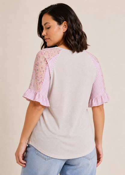 Back view of a woman wearing a blush cross-front tee with floral puff sleeves and light wash denim jeans on a beige background