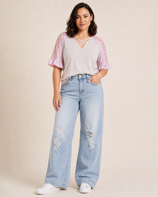 Front view of a woman wearing a blush cross-front tee with floral puff sleeves and light wash denim jeans on a beige background