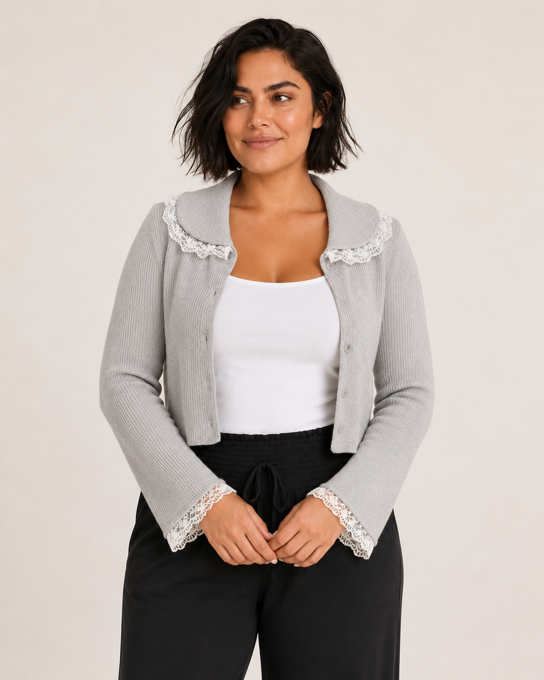 Front view of a woman wearing a gray lace detail flare sleeve knit cardigan with black pants on a beige background