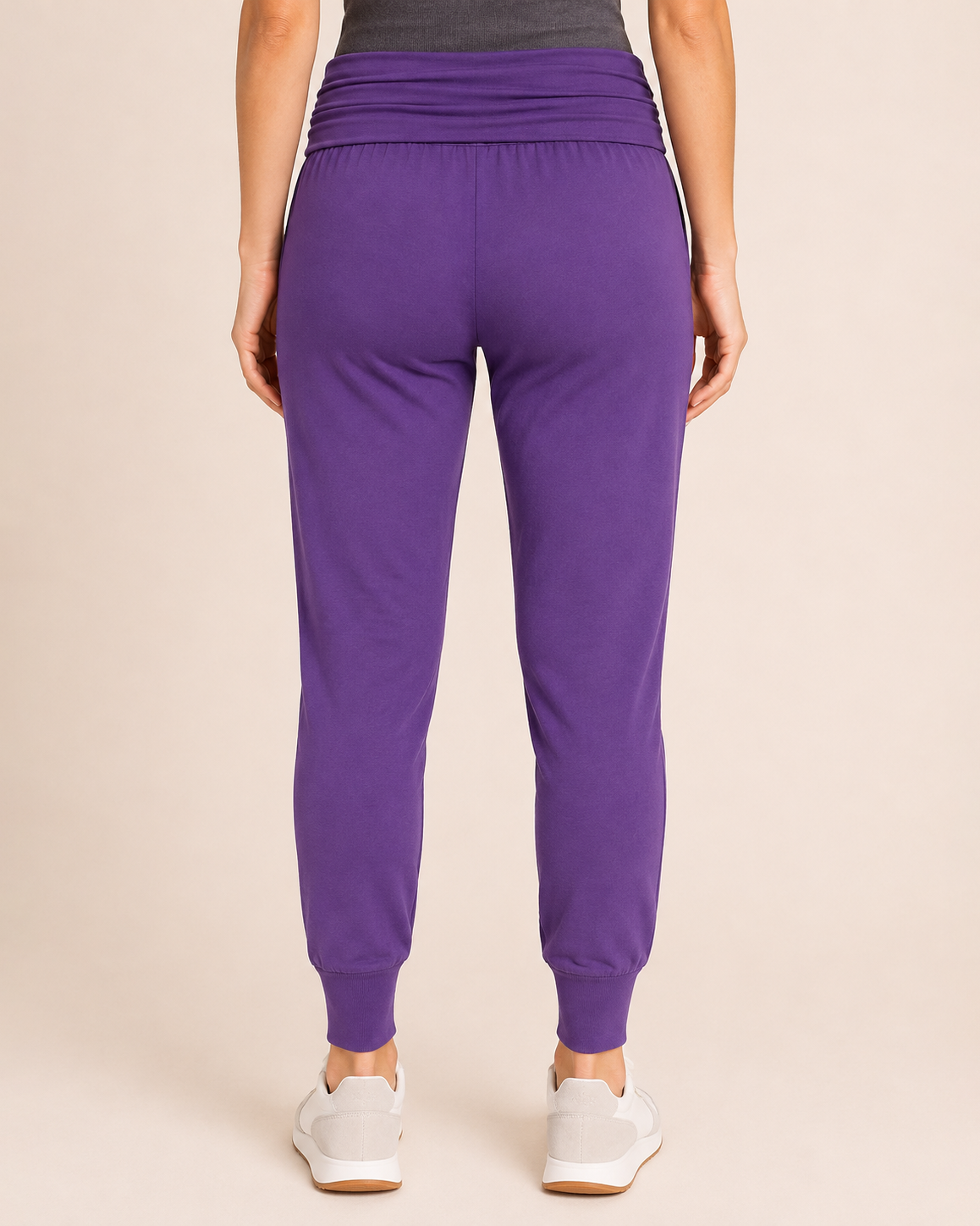 Back view of a woman wearing eggplant foldover waist joggers with white sneakers on a beige background