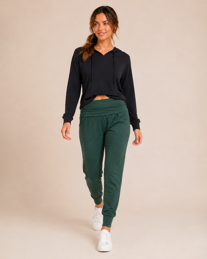 Front view of a woman wearing hunter green foldover waist joggers with white sneakers on a beige background