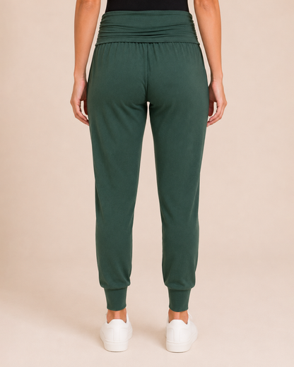 Back view of a woman wearing hunter green foldover waist joggers with white sneakers on a beige background