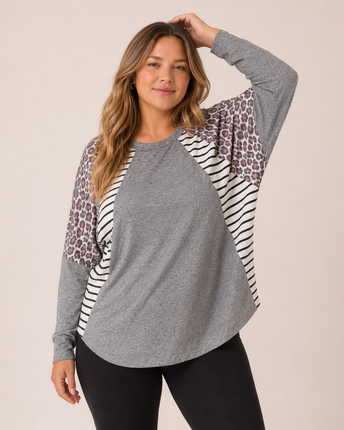 Front view of a woman wearing a gray oversized dolman sleeve tunic with black leggings and white sneakers on a beige background