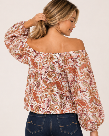 Back view of a woman wearing a floral print top with sheer pleated sleeves and dark blue jeans on a beige background.
