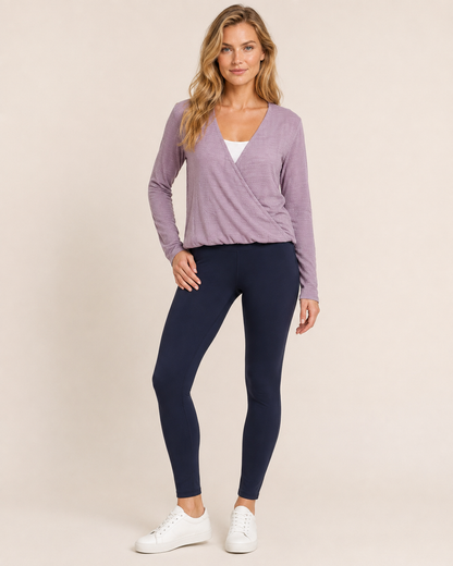 Full-body view of a woman wearing a lilac crossover blouse with black pants and white sneakers on a beige background
