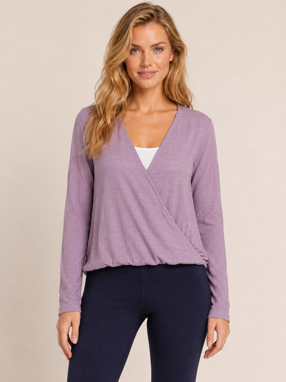 Close-up view of a woman wearing a lilac crossover blouse with black pants on a beige background