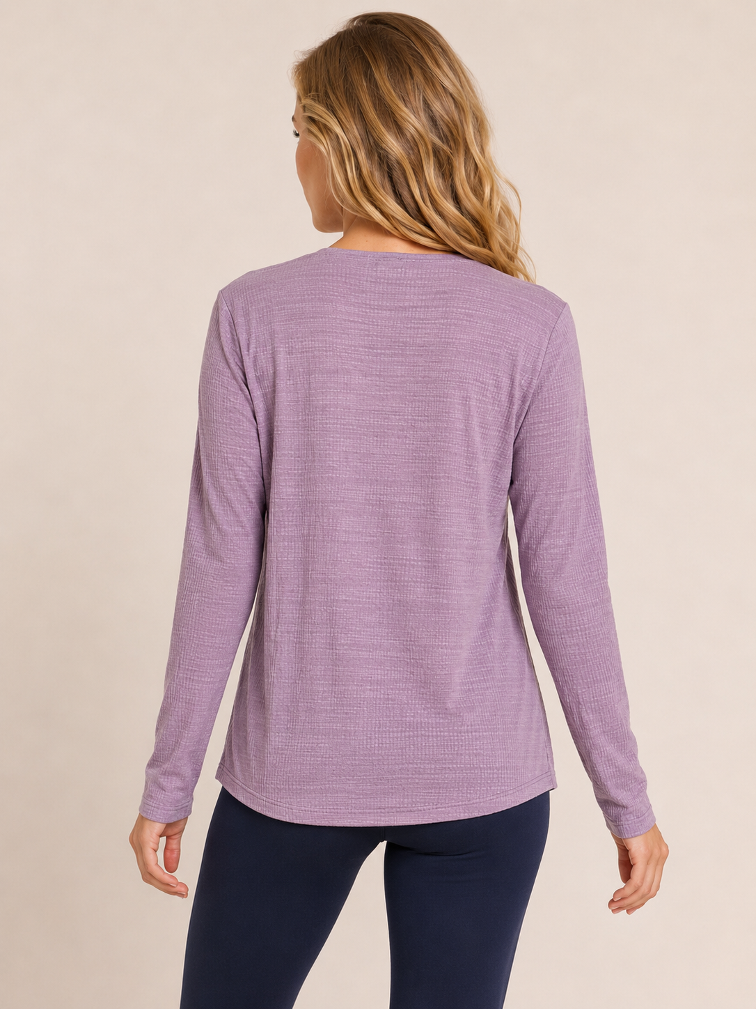 Back view of a woman wearing a lilac crossover blouse with black pants on a beige background