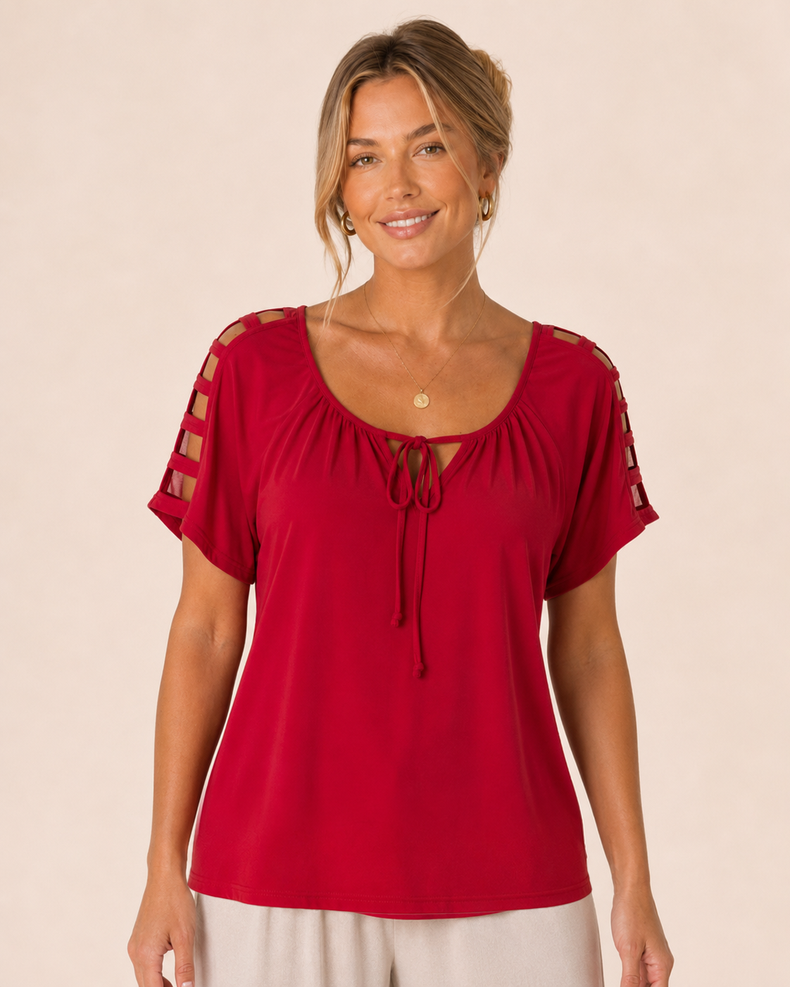 Woman wearing a red short-sleeve top with a gathered neckline and side-tie detail, paired with white wide-leg pants and leopard-print flats on a beige background