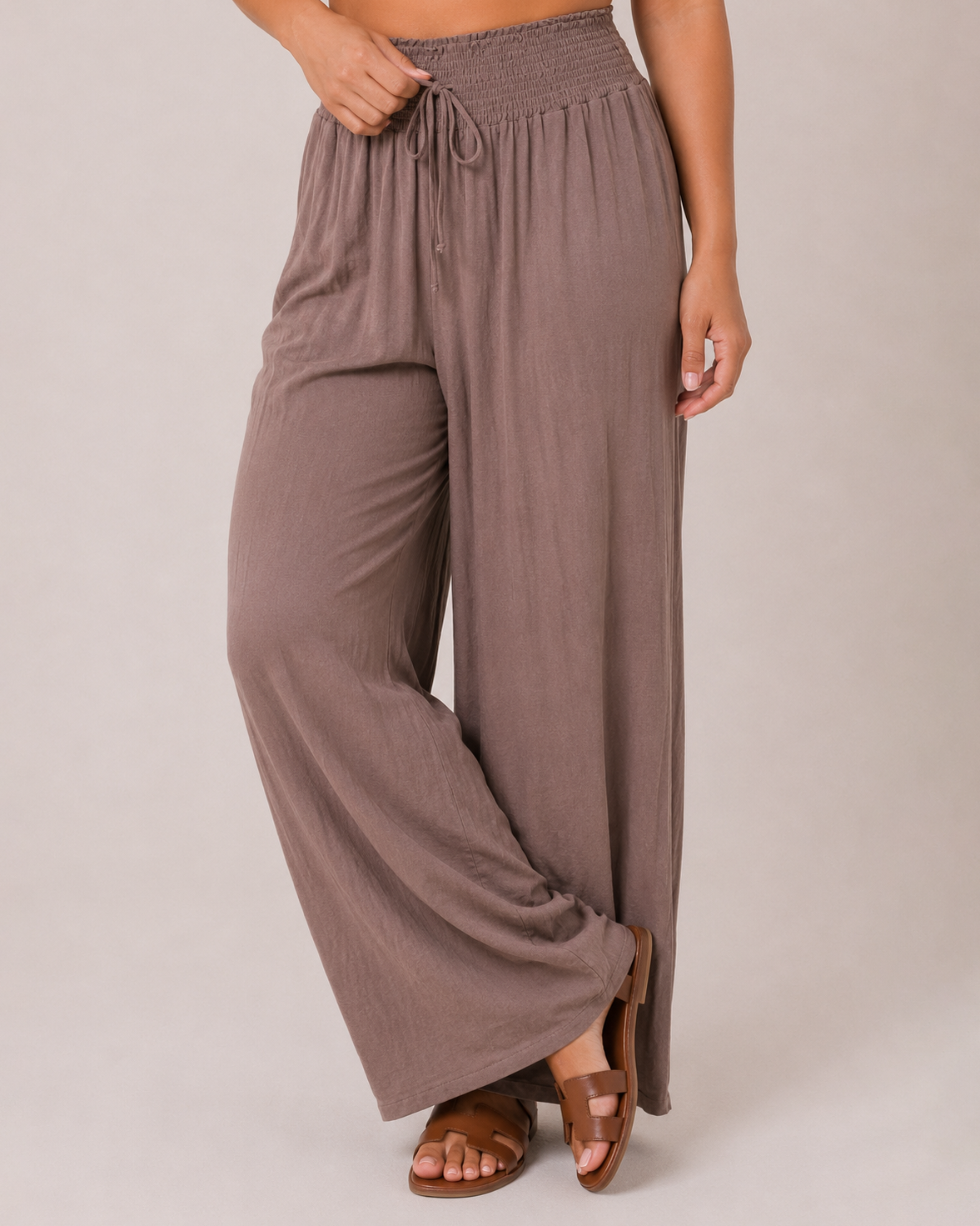 Close-up front view of mocha smocked waist wide-leg pants on a beige background