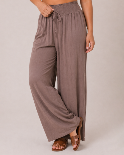 Close-up front view of mocha smocked waist wide-leg pants on a beige background