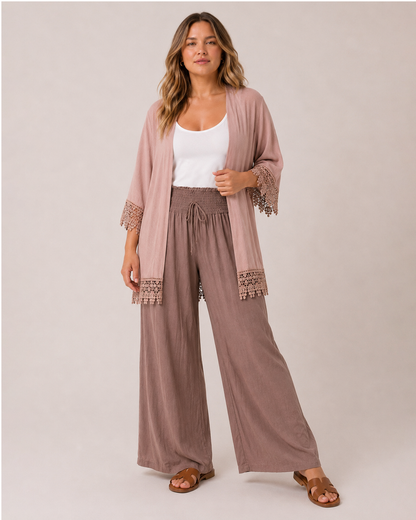 Full-body view of a woman wearing mocha smocked waist wide-leg pants and a white tank top with a taupe kimono.