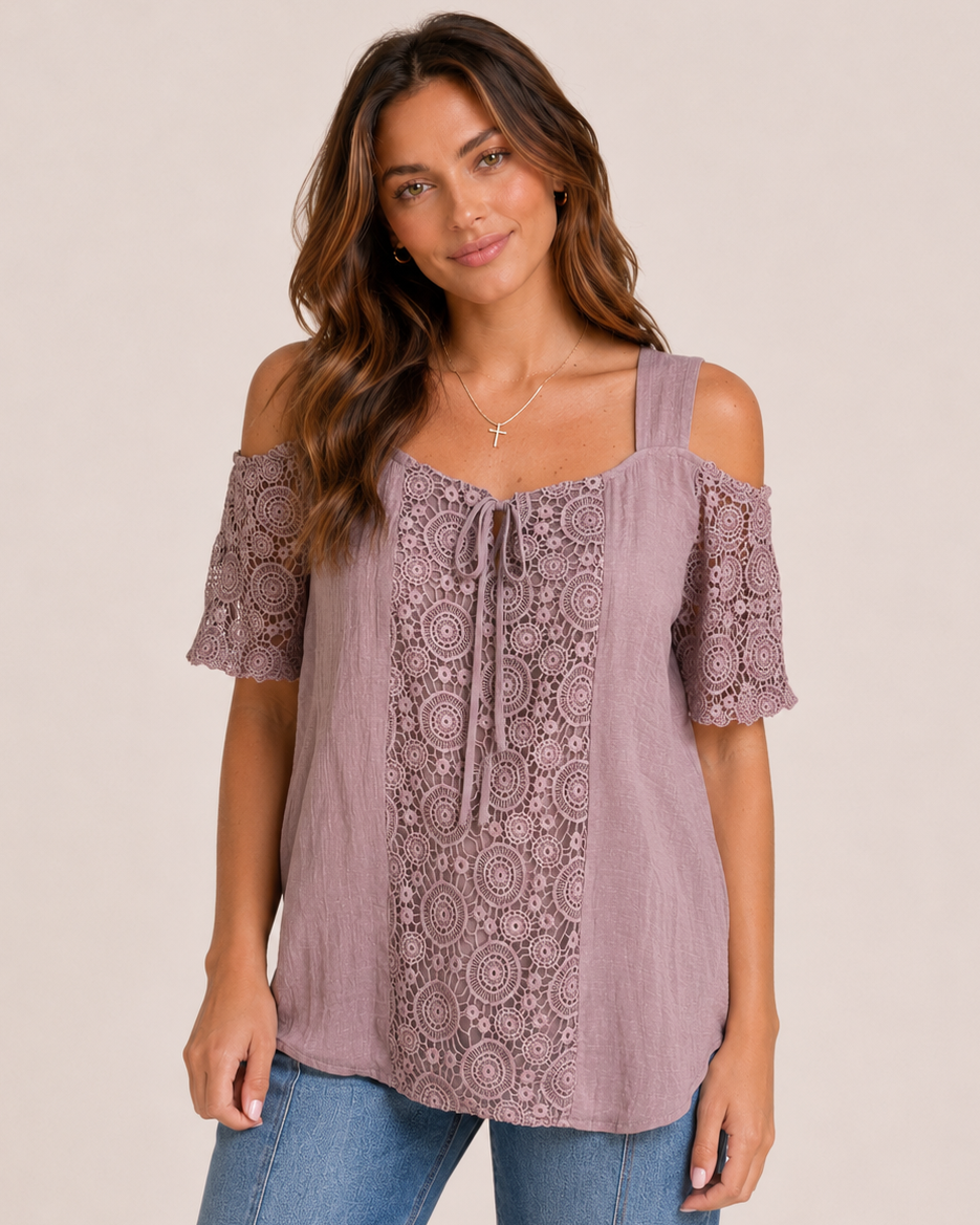 Front view of a woman wearing a mauve cold shoulder lace blouse and cropped blue jeans on a beige background