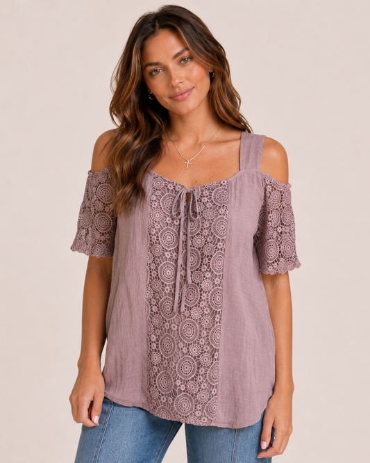 Front view of a woman wearing a mauve cold shoulder lace blouse and cropped blue jeans on a beige background