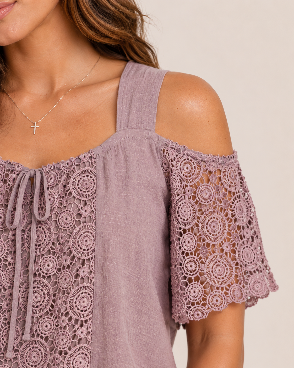 Close-up of a woman wearing a mauve cold shoulder lace blouse on a beige background