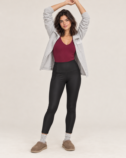 Full-body front view of a woman wearing black high-waisted sculpting leggings with a burgundy tank top and taupe sneakers on a beige background.