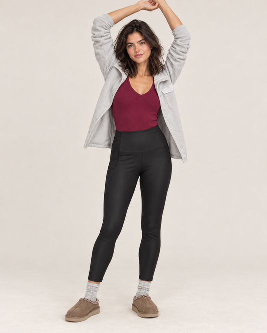 Full-body front view of a woman wearing black high-waisted sculpting leggings with a burgundy tank top and taupe sneakers on a beige background.