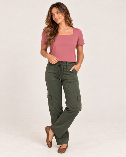 Front view of a woman wearing a muted pink square-neck short-sleeve fitted top with dark olive-green pants on a beige background.