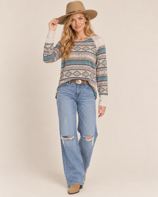 Cropped front view of a woman wearing a multicolor Southwestern geometric-pattern knit sweater with a wide neckline on a beige background.