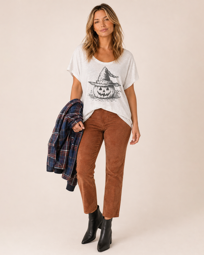 Full-body view of a woman wearing a white pumpkin graphic tee with black pants and black boots on a beige background