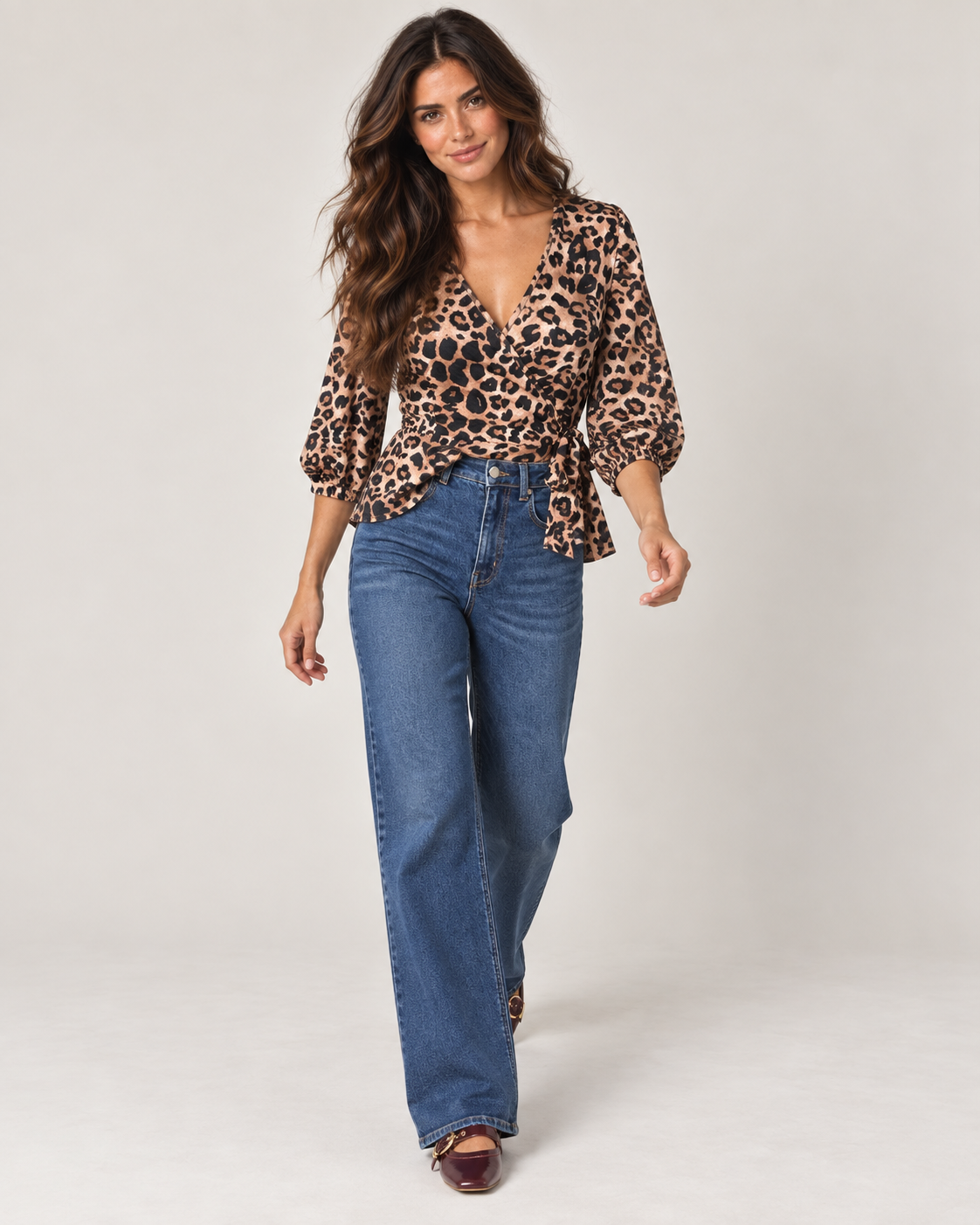 Full-body front view of a woman wearing a leopard print V-neck blouse with long sleeves, brown pants, and dark ankle boots on a beige background.