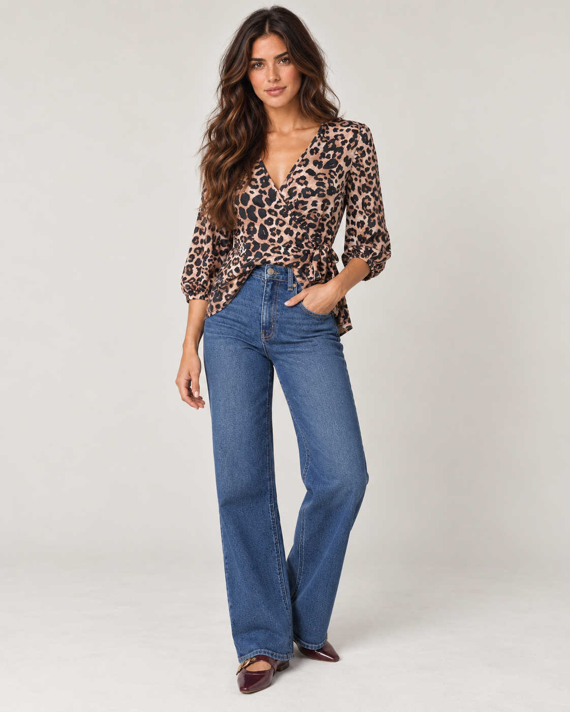 Front view of a woman wearing a leopard print V-neck blouse with long sleeves and blue jeans on a beige background.