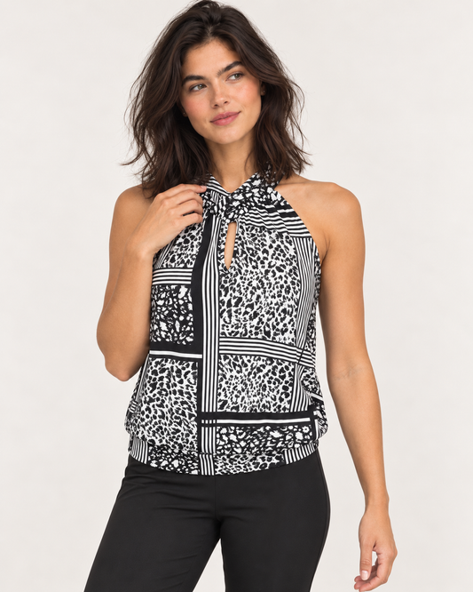 Cropped front view of a woman wearing a black and white patterned sleeveless top with a round neckline and black pants on a beige background.