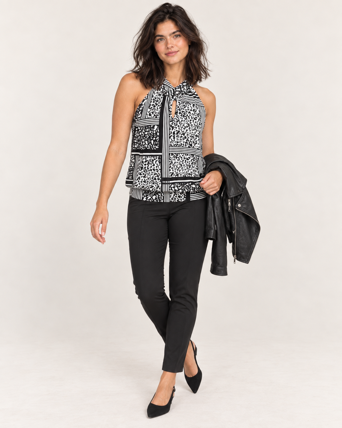 Full-body front view of a woman wearing a black and white patterned sleeveless top with black pants and a gray cardigan draped over her shoulders on a beige background.