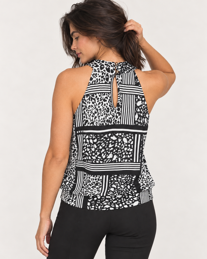 Cropped back view of a woman wearing a black and white patterned sleeveless top with a graphic print on the back and black pants on a beige background.