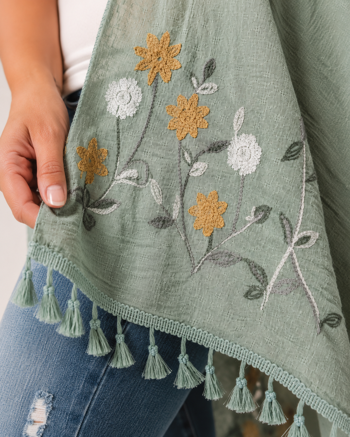 Close-up of a sage embroidered kimono with floral embroidery and tassel trim on a beige background