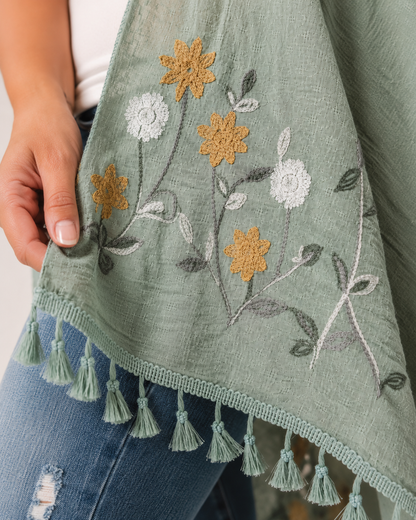 Close-up of a sage embroidered kimono with floral embroidery and tassel trim on a beige background